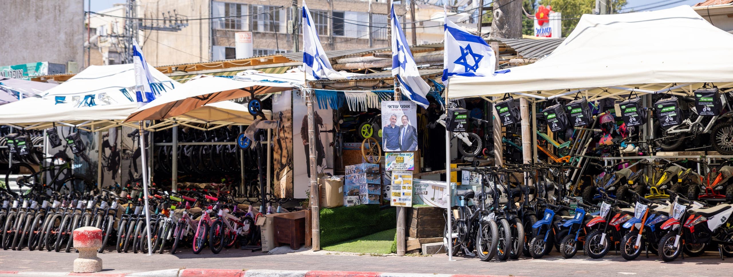 חזית חנות אופני עודאי בדרך מגדיאל 3 בהוד השרון, אופניים וקורקינטים ערוכים לאורך המדרכה